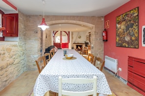 A dining area with a long table, chairs, a fire extinguisher, a fireplace, and a stone wall.