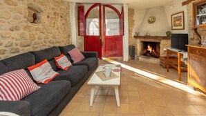 Un salon avec un mur en pierre, une cheminée, un canapé agrémenté de coussins rouges et blancs, et un téléviseur posé sur un meuble en bois.