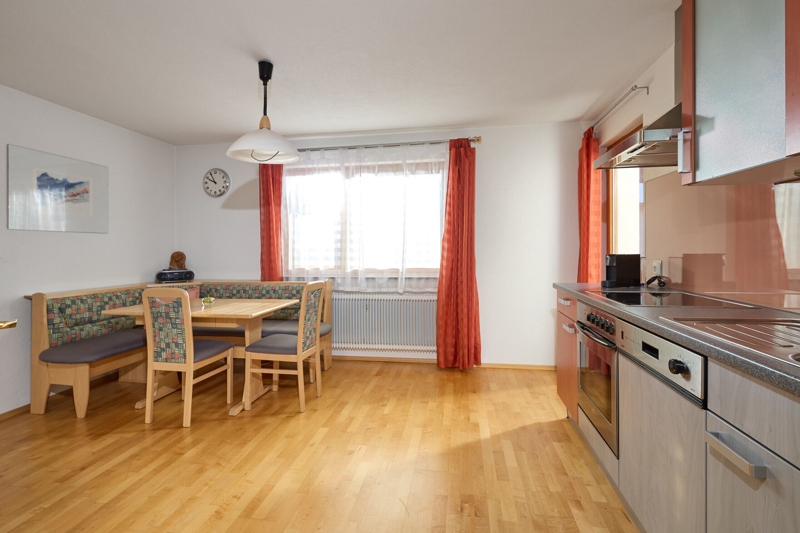 A compact kitchen with a dining area, wooden flooring, and a view of the outdoors.