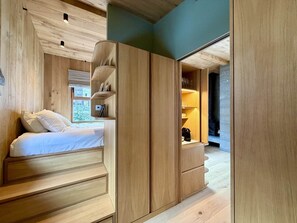 A modern bedroom with a wooden bed, built-in shelves, and a view of the city. - Chalet Meta (Chamonix)
