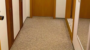 Ein Flur mit einer Holztür, einem Kleiderständer mit Kleiderbügeln und einem gemusterten Teppich.