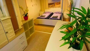 Ein kleines Hotelzimmer mit einem Bett, einem Schreibtisch, einem Kleiderschrank und einer Topfpflanze.