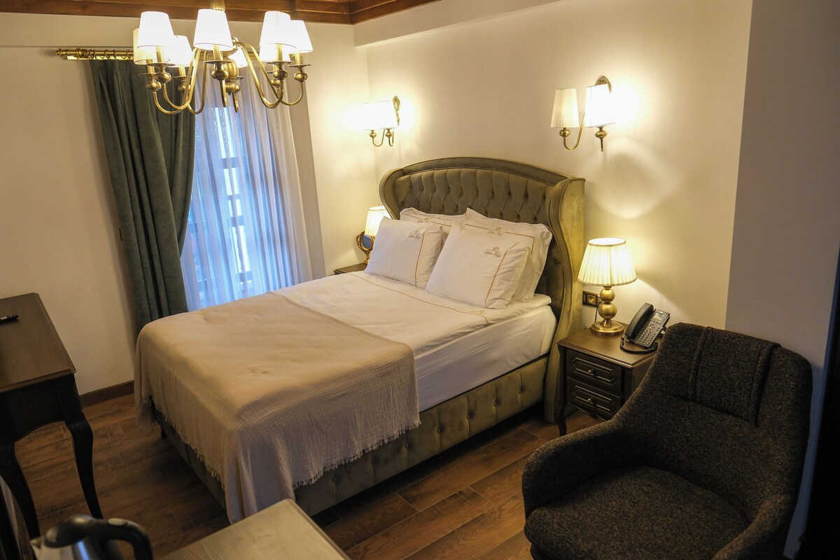 Habitación de hotel con una cama grande, una mesita de noche con lámpara, una silla y un escritorio.