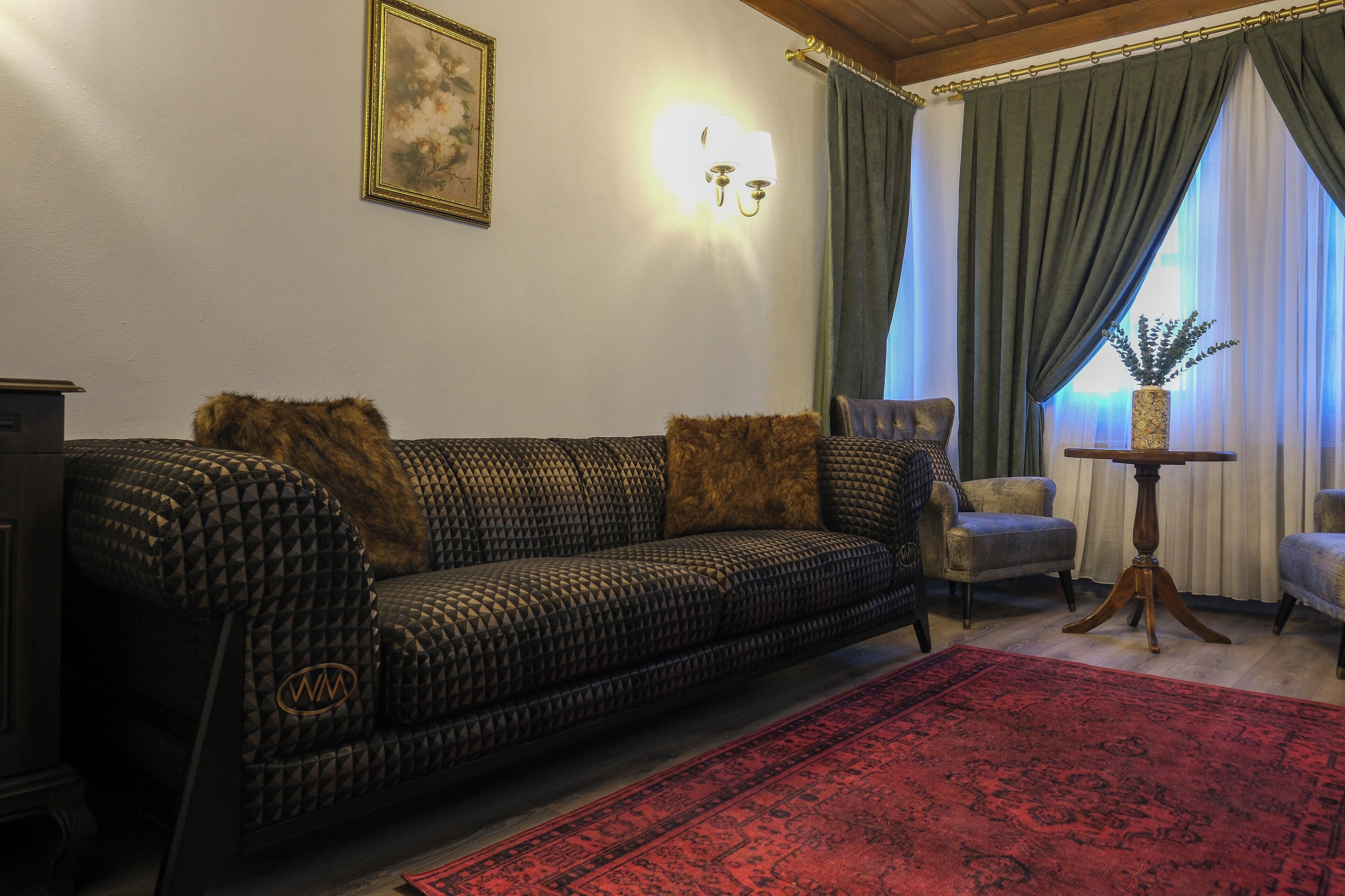 A living room with a patterned sofa, a red rug, a small table with a vase, and a painting on the wall.