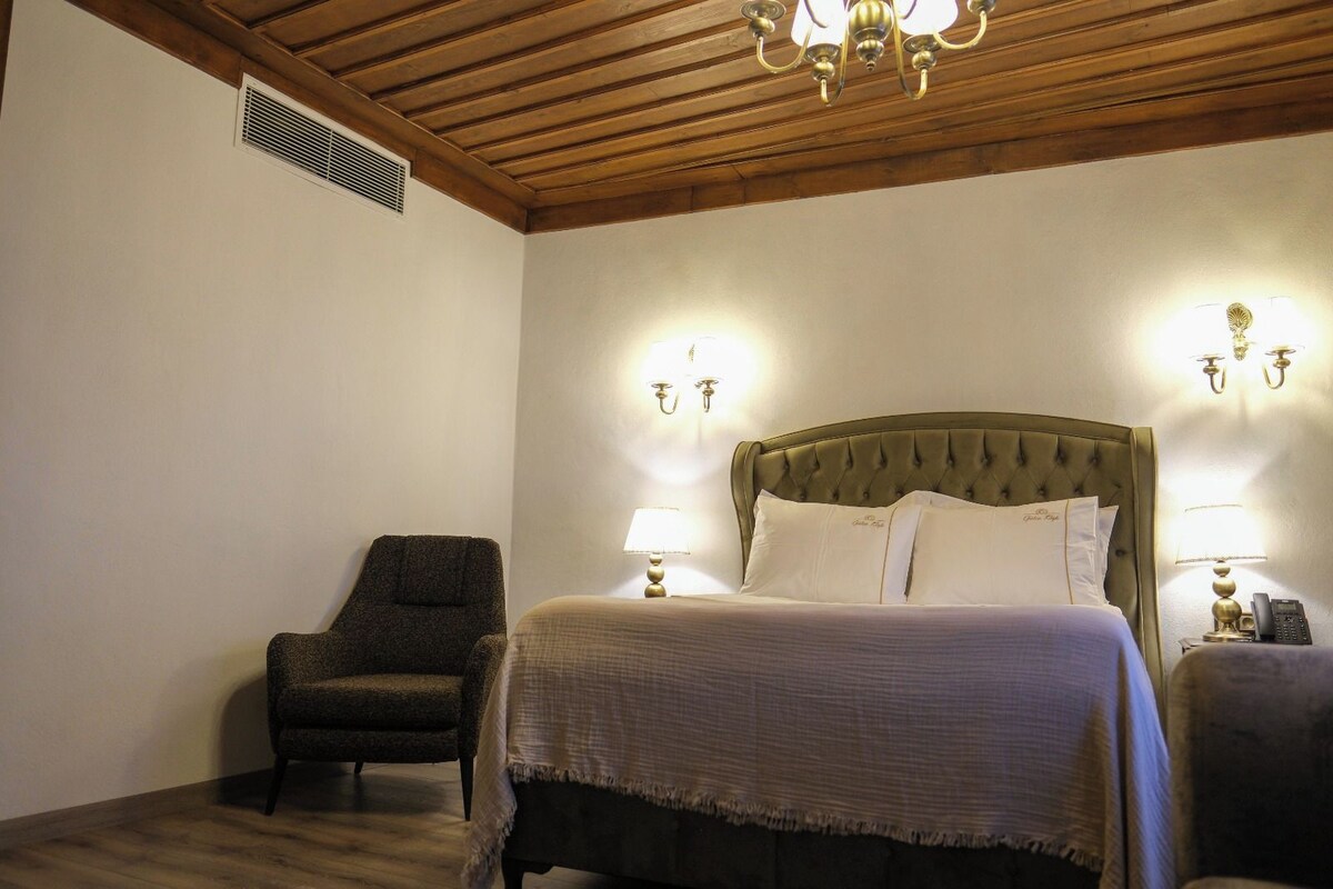 A bedroom with a bed, two bedside lamps, a chair, and a ceiling vent.