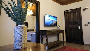 Une pièce avec une table en bois, un vase décoratif contenant une plante, un téléviseur accroché au mur et une porte.