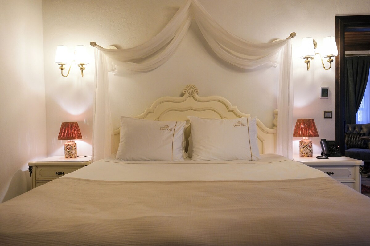Una cama bien hecha con cabecera, dos lámparas de noche y una mesita de noche con lámpara.