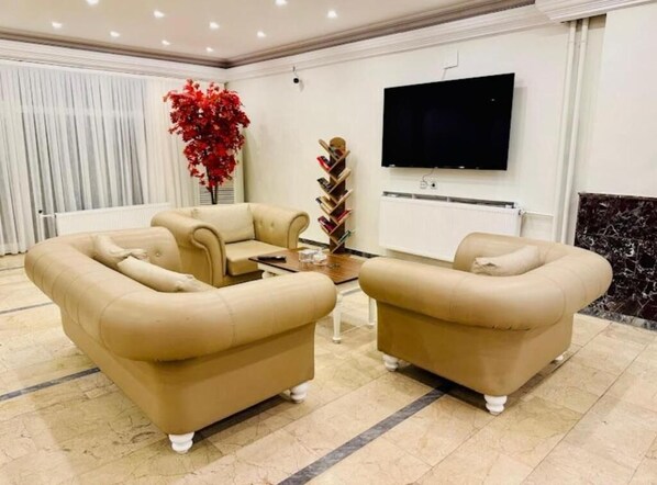 A modern living room with two beige sofas, a coffee table, and a TV mounted on the wall. - GARDEN LİVA HOTEL (Igdir)