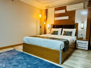 Un dormitorio moderno con una cama de madera, un tapete azul y una mesita de noche con una lámpara.