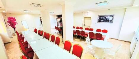 A conference room with a long table and red chairs, a smaller round table with white chairs, and a painting on the wall.