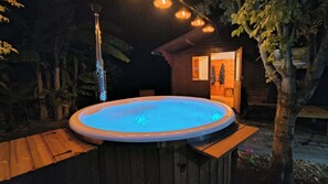 Una vasca idromassaggio all'aperto circondata da un pontile in legno, con una struttura in legno sullo sfondo.