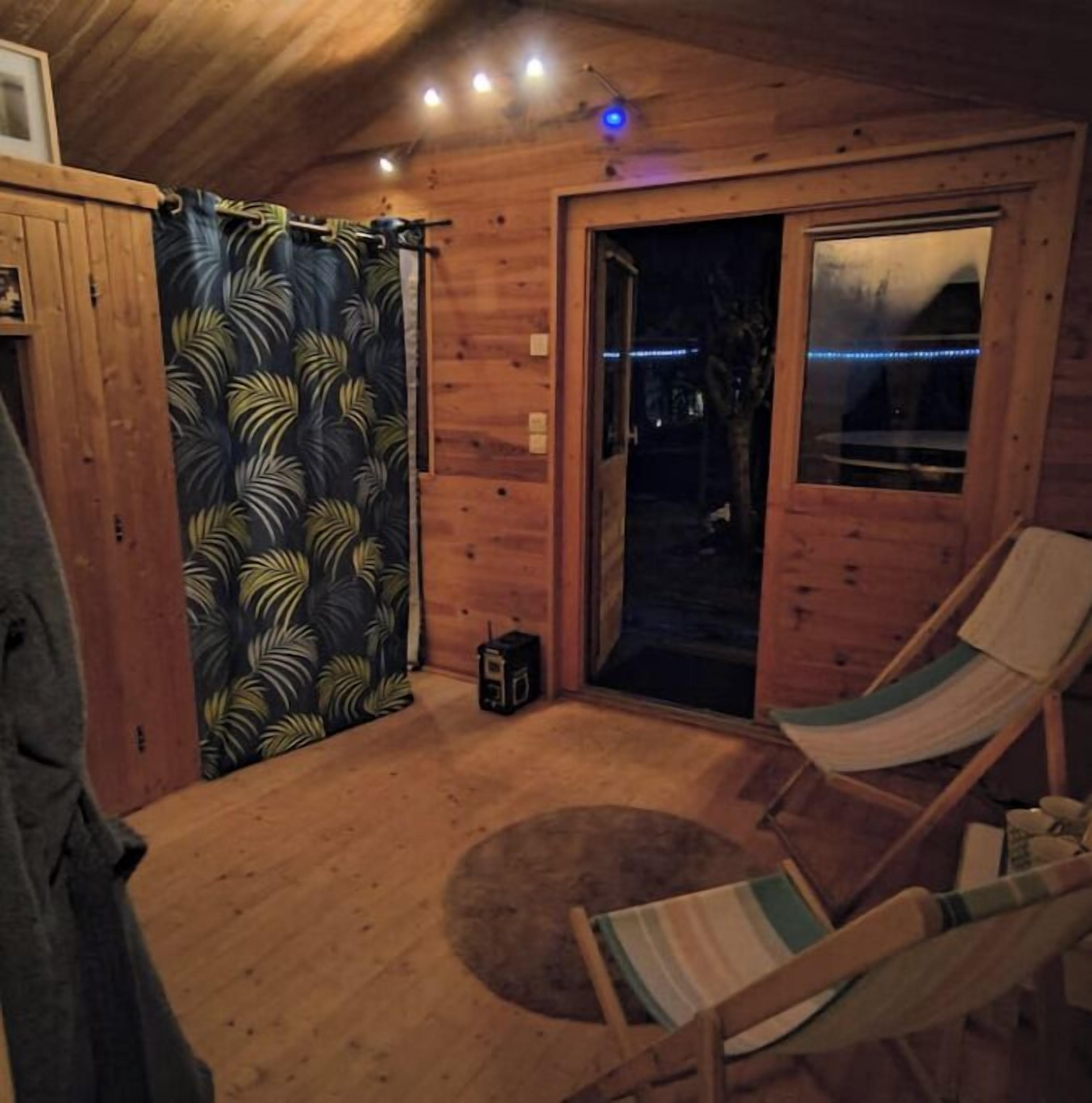 L’intérieur chaleureux d’un chalet avec un plancher en bois, un fauteuil en forme de hamac, une petite table et une porte donnant sur l’extérieur.