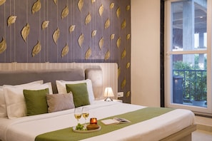 A neatly made bed with pillows, a bedside table with a lamp, a tray with glasses and fruit, and a window with a view of greenery.