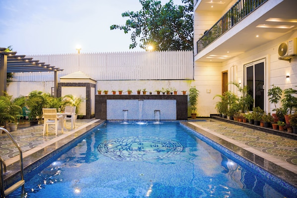 A swimming pool with a decorative tile pattern, surrounded by potted plants and outdoor furniture.