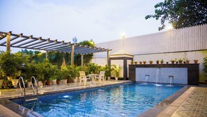 A swimming pool with a pergola, lounge chairs, and potted plants. - Alaya Stays Versace Farms |5 BHK Farm house (Noida)