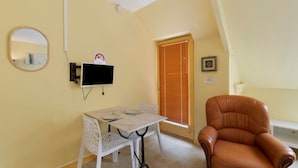 A room with a single table, a chair, a television mounted on the wall, a door with blinds, and a framed picture on the wall. - Apartment "Les Moulins - Studio 1" with Balcony and Wi-Fi (Cherbourg en Cotentin)