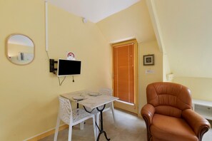 Ein Zimmer mit einem Tisch, einem Stuhl, einem an der Wand montierten Fernseher, einer Tür mit Jalousien und einem gerahmten Bild.