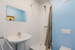 A bathroom with a white sink, a mirror, a shower with a beige curtain, and a blue wall. - Apartment "Les Moulins - Studio 1" with Balcony and Wi-Fi (Cherbourg en Cotentin)