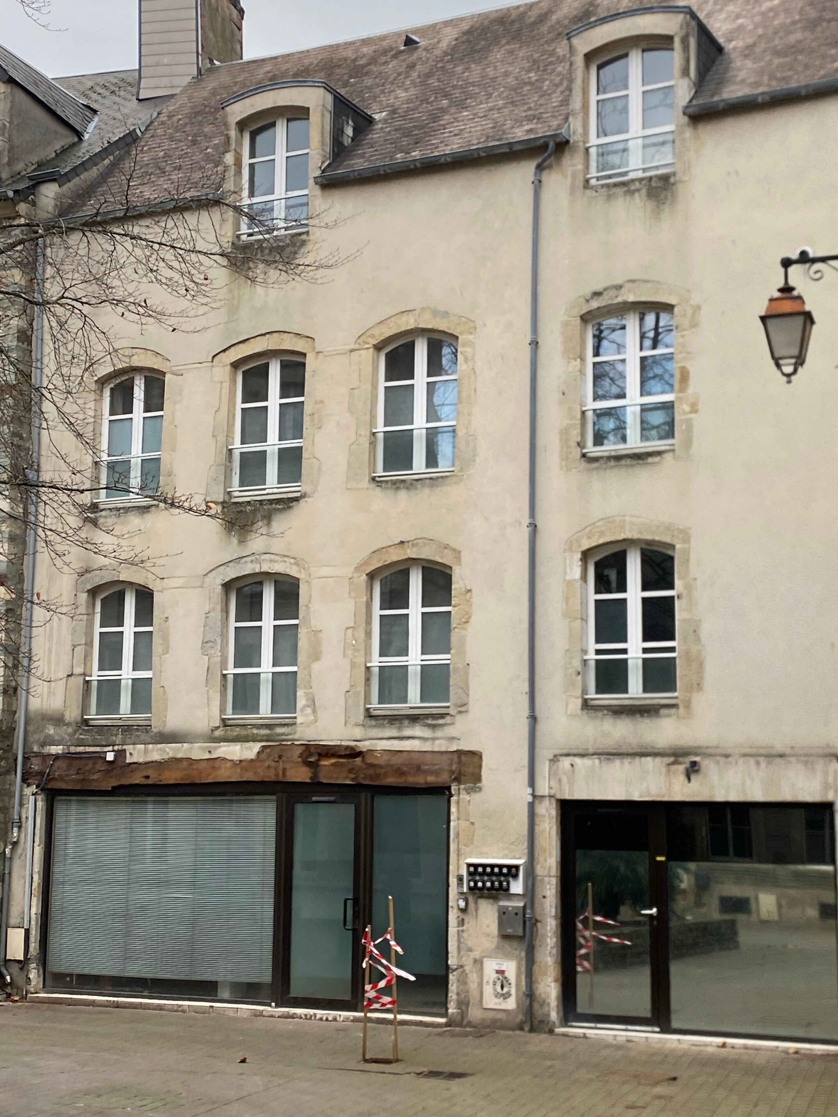 A multi-story building with arched windows, a closed shuttered entrance, and a street lamp.