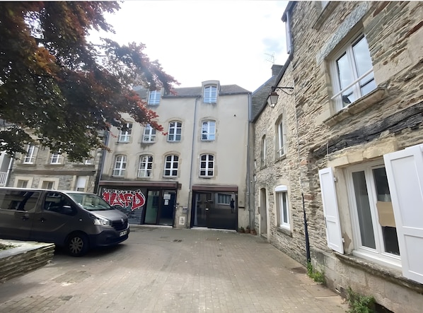 Une rue étroite bordée d’immeubles en pierre, une voiture garée et une devanture de magasin bien visible avec une enseigne.