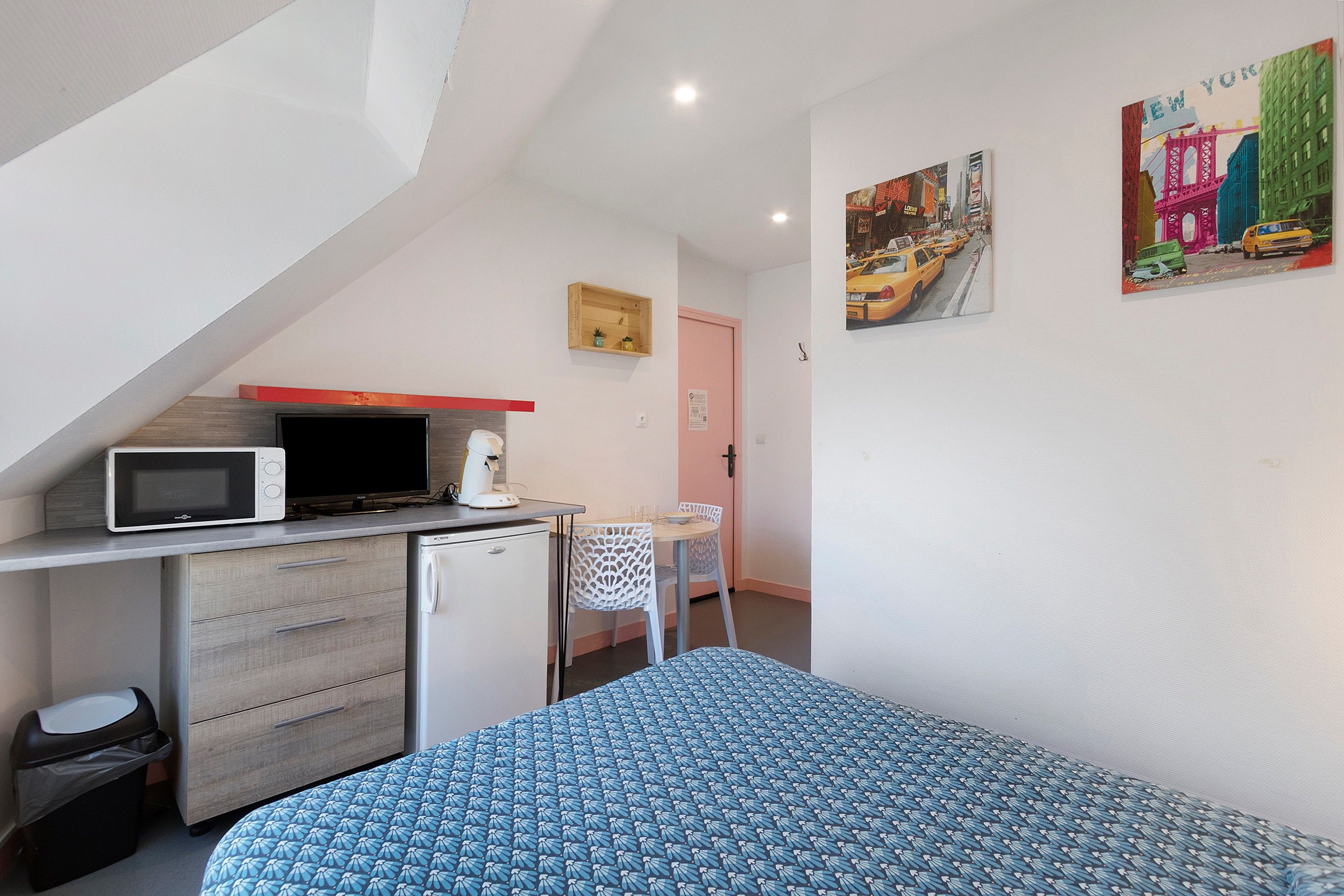 A compact room with a kitchenette, a bed, a small table, and chairs.