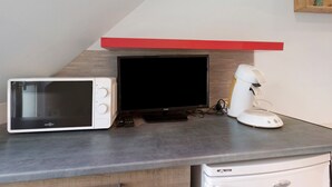 Ett litet kök med mikrovågsugn, tv och kaffebryggare på en bänkskiva.