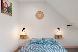 Ein Schlafzimmer mit einem Bett, zwei Nachttischen, einer Wandleuchte, einem runden Wandbild und einer kleinen Pflanze auf einem der Tische.