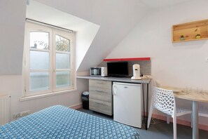 Une pièce de taille modeste comprenant un lit, un bureau, un four à micro-ondes, un réfrigérateur et une fenêtre.