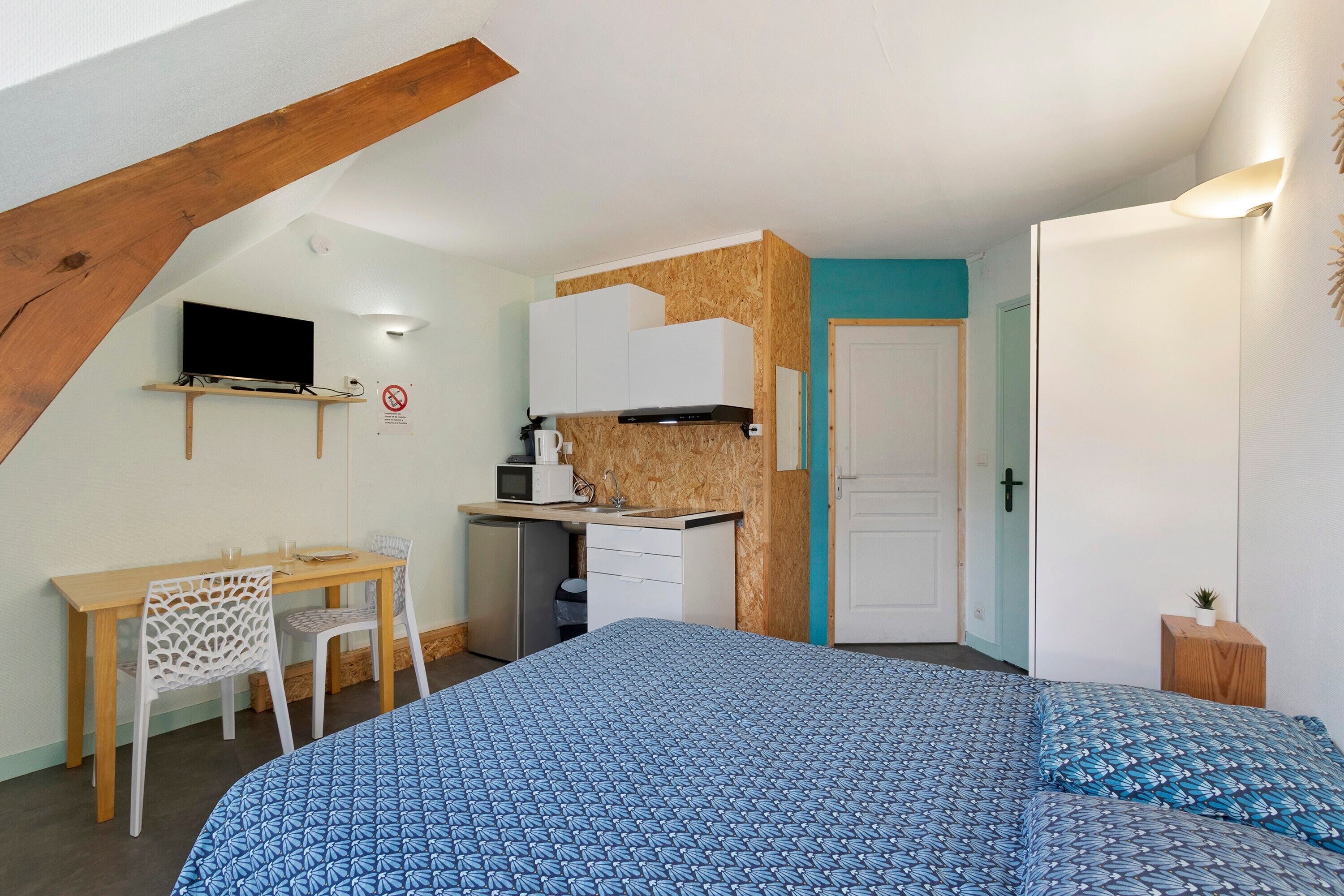 A compact bedroom with a bed, a desk, and a kitchenette.