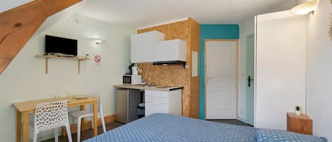 A compact bedroom with a bed, a desk, and a kitchenette.