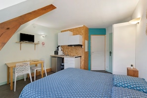 Une chambre compacte comprenant un lit, un bureau et un coin cuisine.