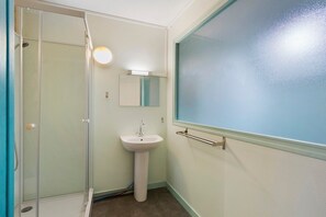 Une salle de bain avec une douche à parois de verre, un lavabo blanc et une fenêtre teintée de bleu.