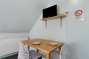 Un petit coin repas avec une table, des chaises, un téléviseur fixé à une étagère et un panneau «interdiction de fumer» sur le mur.