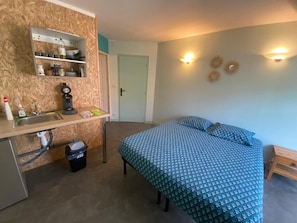 Une petite pièce comprenant un lit, un petit bureau avec un lavabo, un miroir et une porte donnant sur une autre pièce.