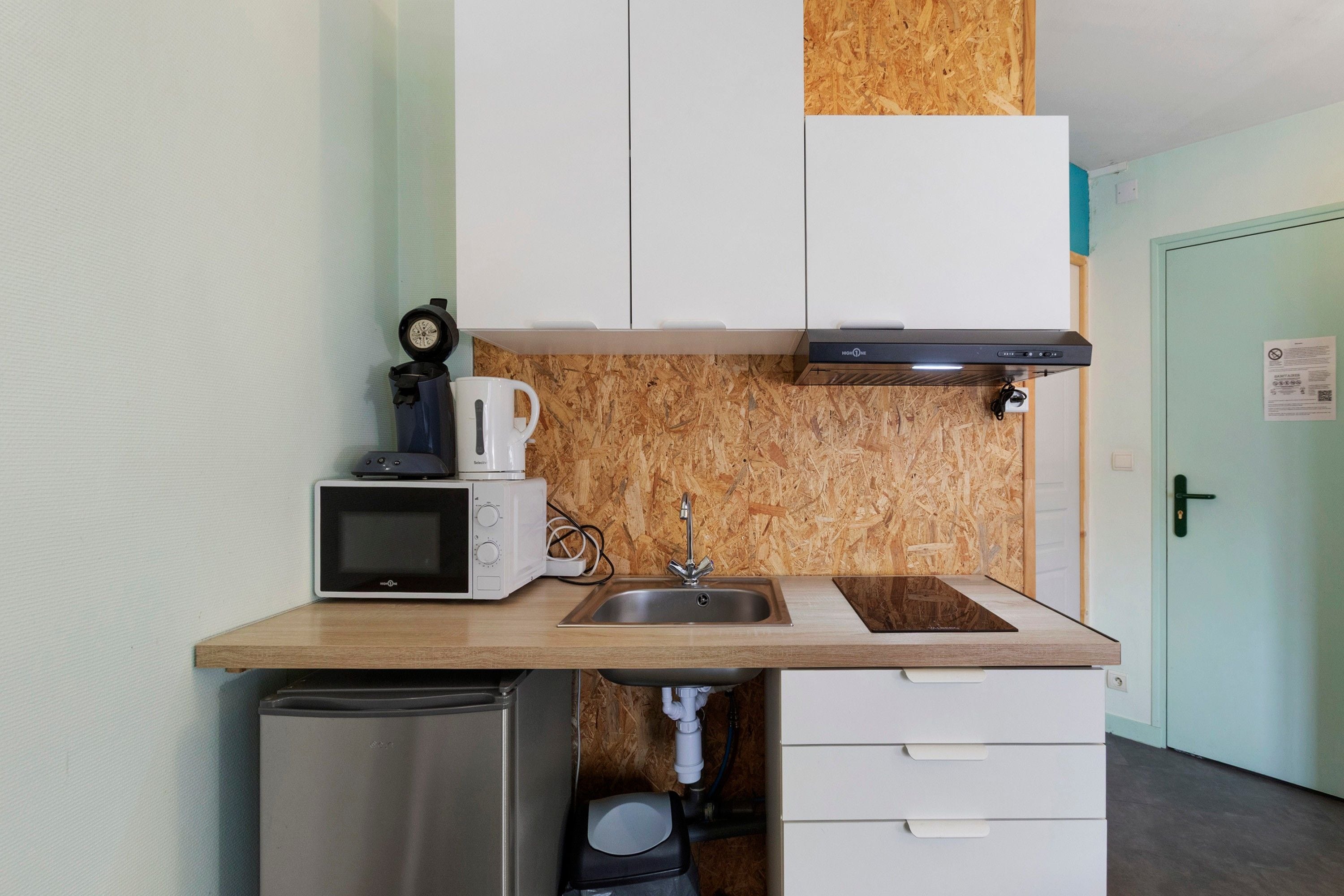 Una kitchenette compacta equipada con microondas, cafetera y un lavamanos pequeño.