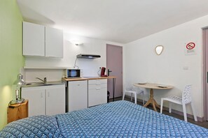A compact hotel room with a kitchenette, a bed with a patterned duvet, a small dining table with chairs, and a mirror on the wall. - Les Moulins - Studio 6 Apartment with Wi-Fi (Cherbourg en Cotentin)