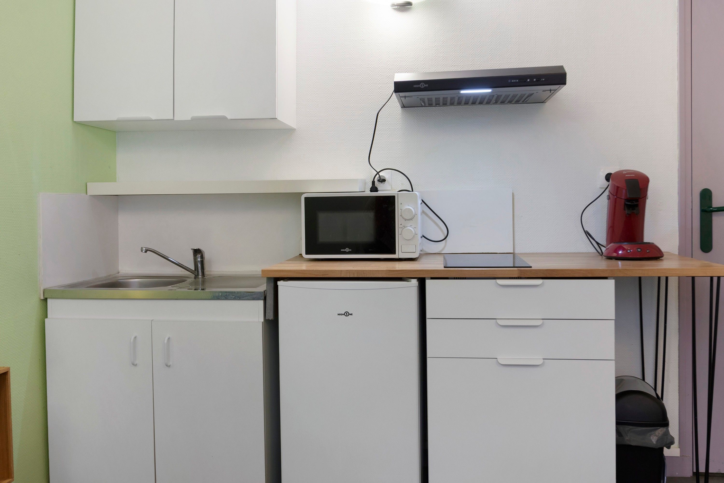 Une petite cuisine équip ée comprenant un four à micro-ondes, un petit réfrigérateur, un évier et une machine à café rouge posée sur le plan de travail.