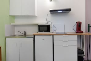 A compact kitchenette with a microwave, a small refrigerator, a sink, and a red coffee maker on the countertop.