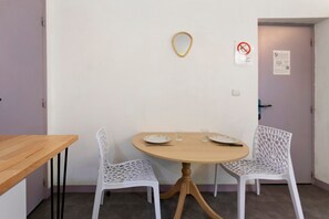 A small dining area with a round table, two white chairs, and a wooden side table.