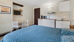 Una stanza compatta con un letto, una scrivania, una sedia, angolo cottura e una porta.