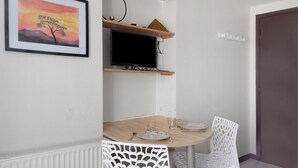 Una stanza con un tavolo da pranzo, sedie, un quadro incorniciato, un televisore e una porta.