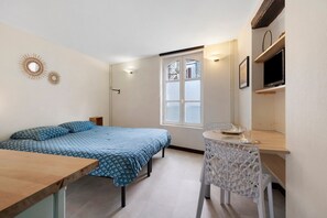 Un dormitorio con cama, escritorio, silla, ventana y televisor.