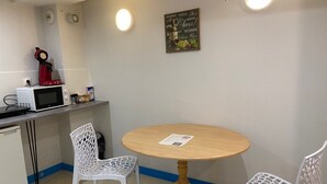 A small kitchenette with a microwave, a red coffee maker, and a white chair. There is a round wooden table with a white chair in front. - Apartment 'Les Moulins - 8' with Wi-Fi (Cherbourg en Cotentin)