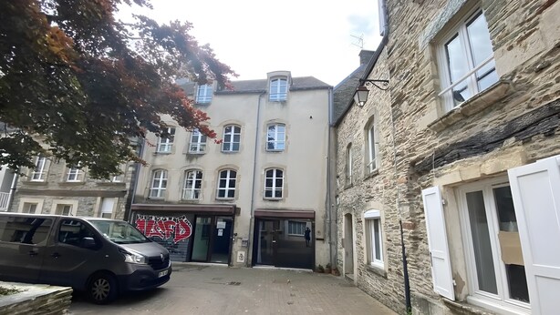 A narrow street with stone buildings, a parked car, and a visible storefront with a sign. - Apartment 'Les Moulins - 8' with Wi-Fi (Cherbourg en Cotentin)