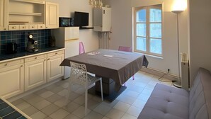 A compact living space with a kitchenette, a dining table, a sofa, and a large window providing natural light. - Apartment 'Les Moulins - T2 - 4' with Wi-Fi (Cherbourg en Cotentin)