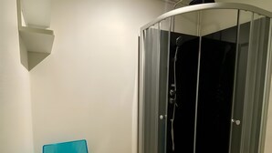 A corner shower enclosure with a glass door, a blue chair, and a small mat. - Apartment 'Les Moulins - T2 - 4' with Wi-Fi (Cherbourg en Cotentin)