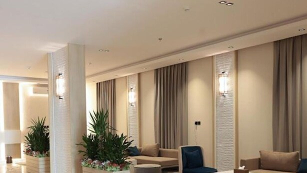 Een moderne lobby met een bank, fauteuils en een salontafel, met een kamerbreed tapijt en decoratieve planten.