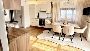 Una cocina moderna con armarios de madera, una zona de comedor con alfombra blanca y un ventanal con cortinas.