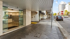 A modern building with a glass facade, a visible entrance, and a street view with cars and buildings in the background. - Chic Studio With a Pool and Moments From Shop (Sydney)