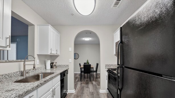 A kitchen with white cabinets, a black refrigerator, and a granite countertop. - Spacious condo near Atlanta with great sleep (Stockbridge)
